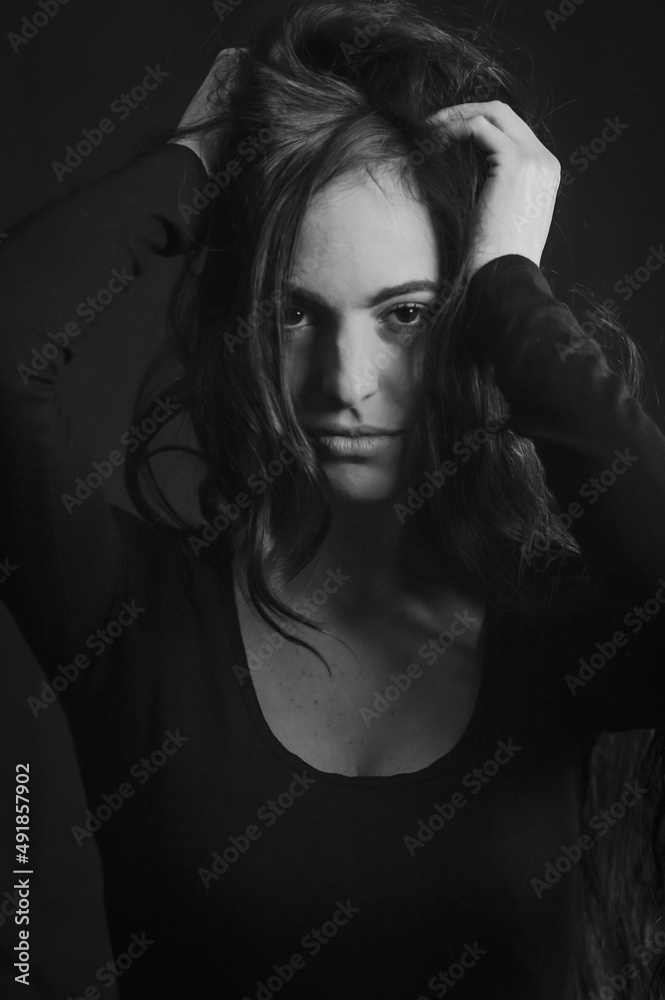 Black and white portrait of a beautiful long-haired Italian woman who, with her hands on her head, has an intense and seductive gaze