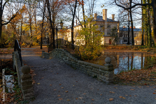 Historyczny park pałacowy jesienią z widocznymi budynkami mieszkalnymi i gospodarczymi.