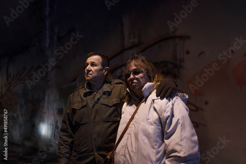 Elderly wife and husband standing together in an abandoned nuclear shelter