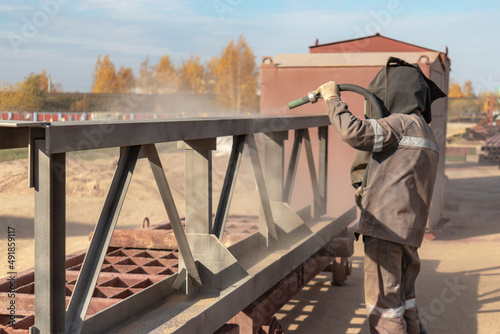 Canvas Print A worker in special clothing is sandblasting a metal building structure at an industrial site