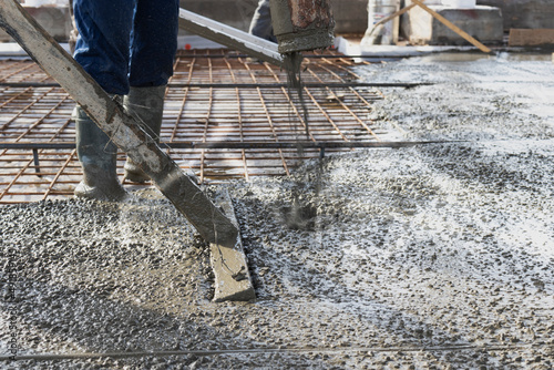 Builders workers pour concrete floor in industrial workshop. Legs in boots in concrete. Submission of concrete for pouring the floor. Monolithic concrete works.