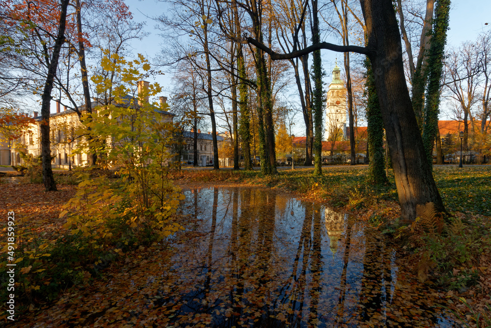 Historyczny park pałacowy jesienią z widocznymi budynkami mieszkalnymi i gospodarczymi.
