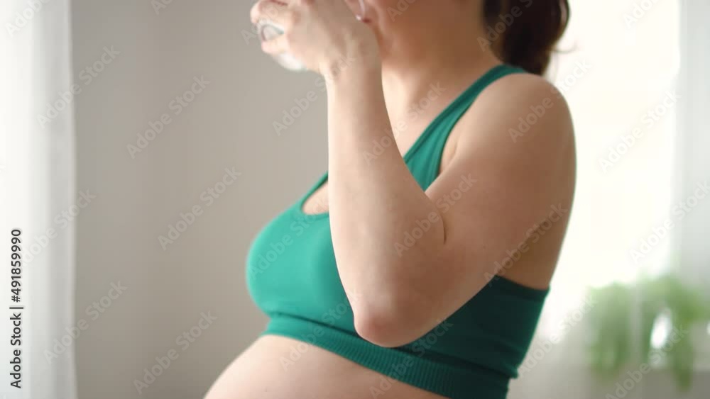Pregnant woman holds a glass of water in her hand. Focus in the foreground on the water. The concept of a healthy lifestyle, support for water balance, proper nutrition during pregnancy. Pregnant woman holds a glass of water in her hand. Focus in the foreground on the water. The concept of a healthy lifestyle, support for water balance, proper nutrition during pregnancy.