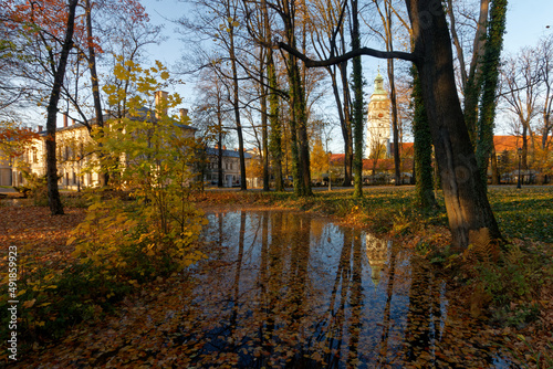 Historyczny park pałacowy jesienią z widocznymi budynkami mieszkalnymi i gospodarczymi.