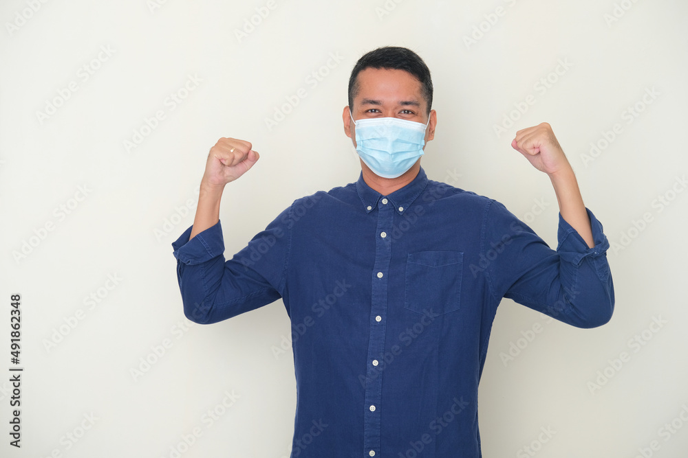 Adult Asian man wearing medical mask showing his bicep muscle. Health concept Adult Asian man wearing medical mask showing his bicep muscle. Health concept
