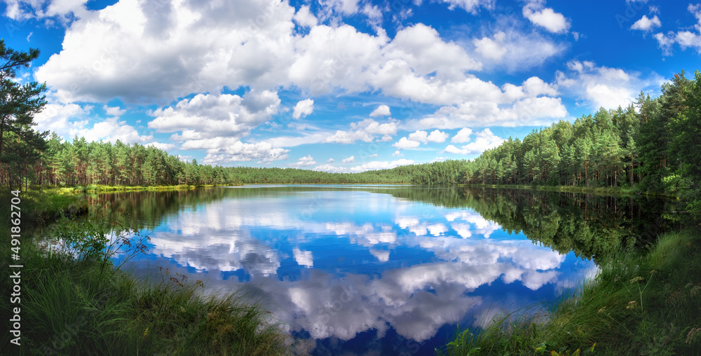 Beautiful natural morning landscape with a lake against backdrop of blue sky with clouds.