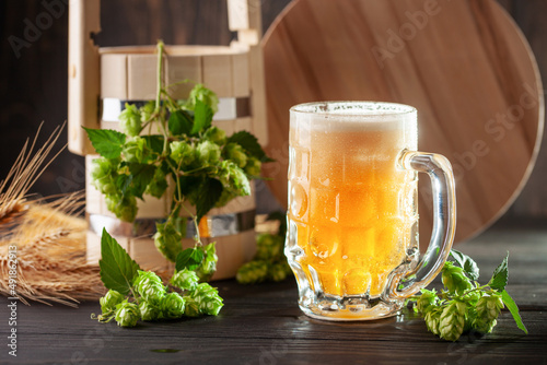 Glass of beer on wooden table with wheat ears and hop cones
