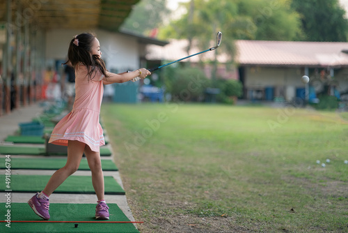 young girl practices her golf swing on driving range