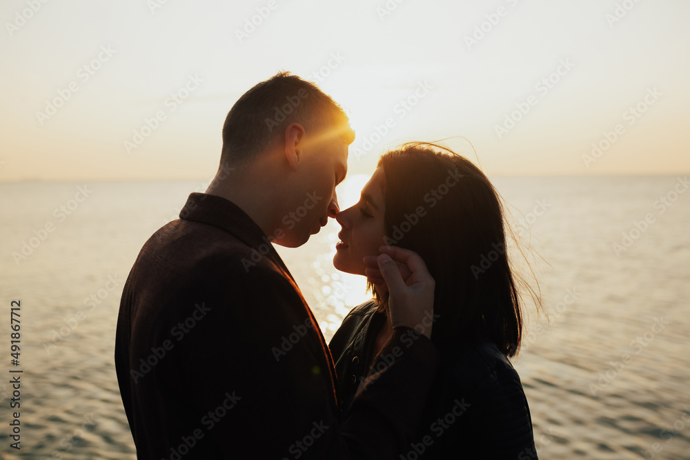 Close-up of sensual beautiful young couple hugging while standing on the sea beach at sunset.