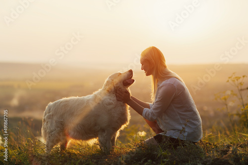 Obraz na płótnie Happy young woman is sitting on the hill at sunset lovingly hugging her large breed dog. w salonie