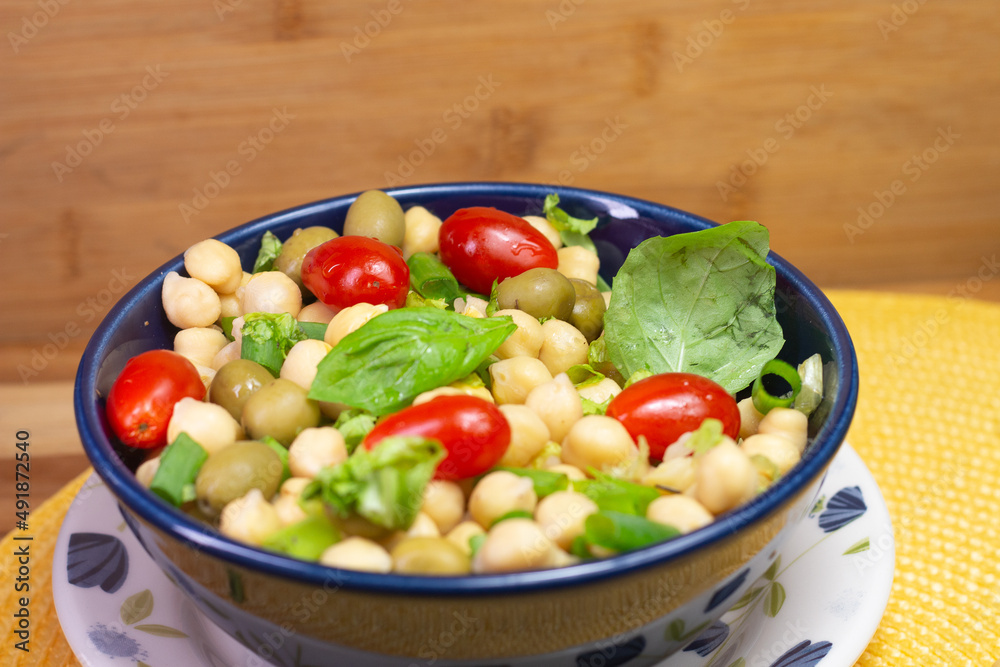 spoon with chickpeas with leaves, olives and tomatoes in a blue bowl on the table