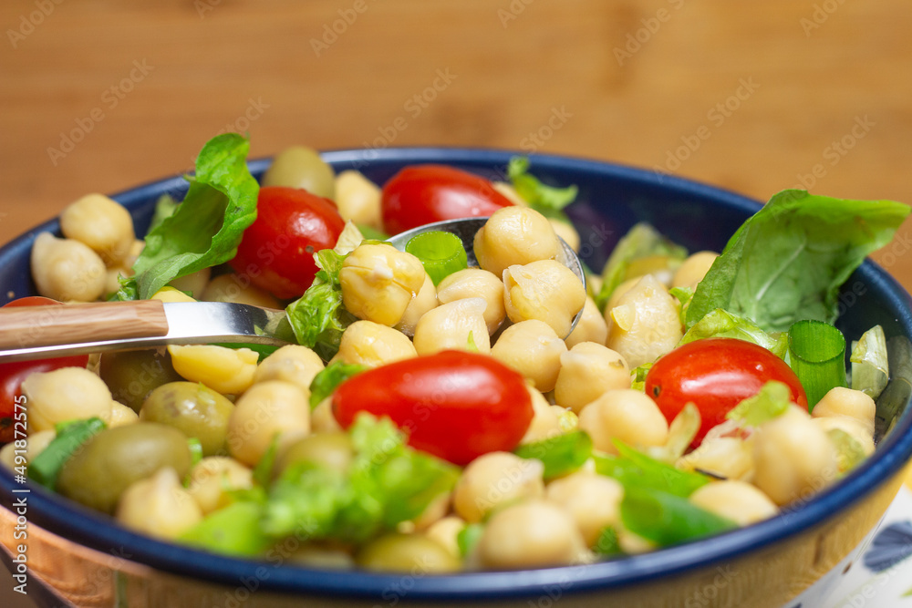 spoon with chickpeas with leaves, olives and tomatoes in a blue bowl spoon with chickpeas with leaves, olives and tomatoes in a blue bowl