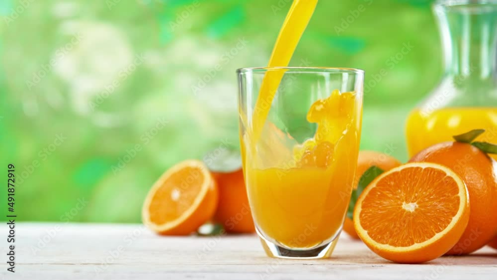 Super slow motion of pouring orange juice into glass. Placed on white table with abstract green background. Filmed on high speed cinema camera, 1000 fps. Speed ramp effect. Super slow motion of pouring orange juice into glass. Placed on white table with abstract green background. Filmed on high speed cinema camera, 1000 fps. Speed ramp effect.