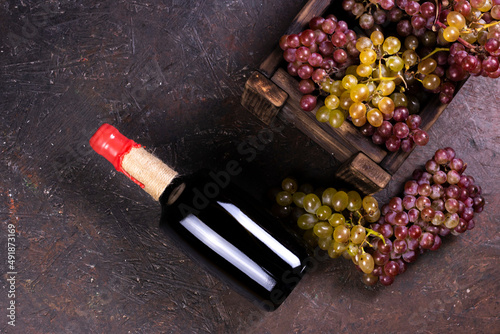 Ripe sweet grapes in wooden box and wine bottle on dark background. Flat lay, top view image with copy space.