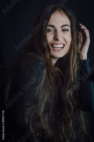 Portrait of a beautiful young woman with very long hair who laughs cheerfully and brings her hand close to her head