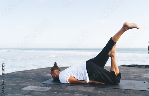 Flexible man in active wear enjoying recreation during yoga workout at embankment, Caucasian male on sportive mat doing stretching asana reaching vitality and balance during morning training