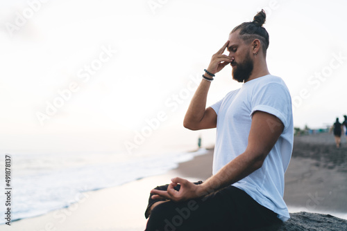 Calm Caucasian man keep praying during daytime for pranayama at seashore enjoying leisure in Indonesia, young male yogi meditate in lotus pose searching soul enlightenment and mindfulness