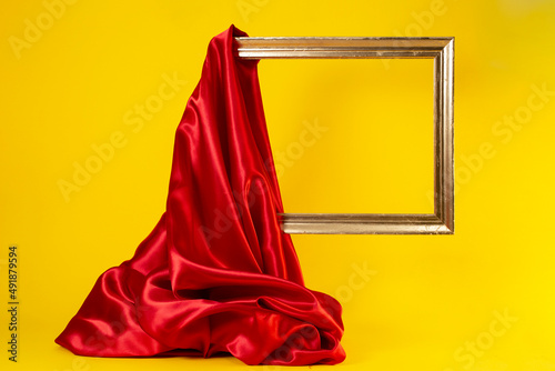 Fotografie Levitating golden frame, being unveiled with a red satin cloth, isolated on yell
