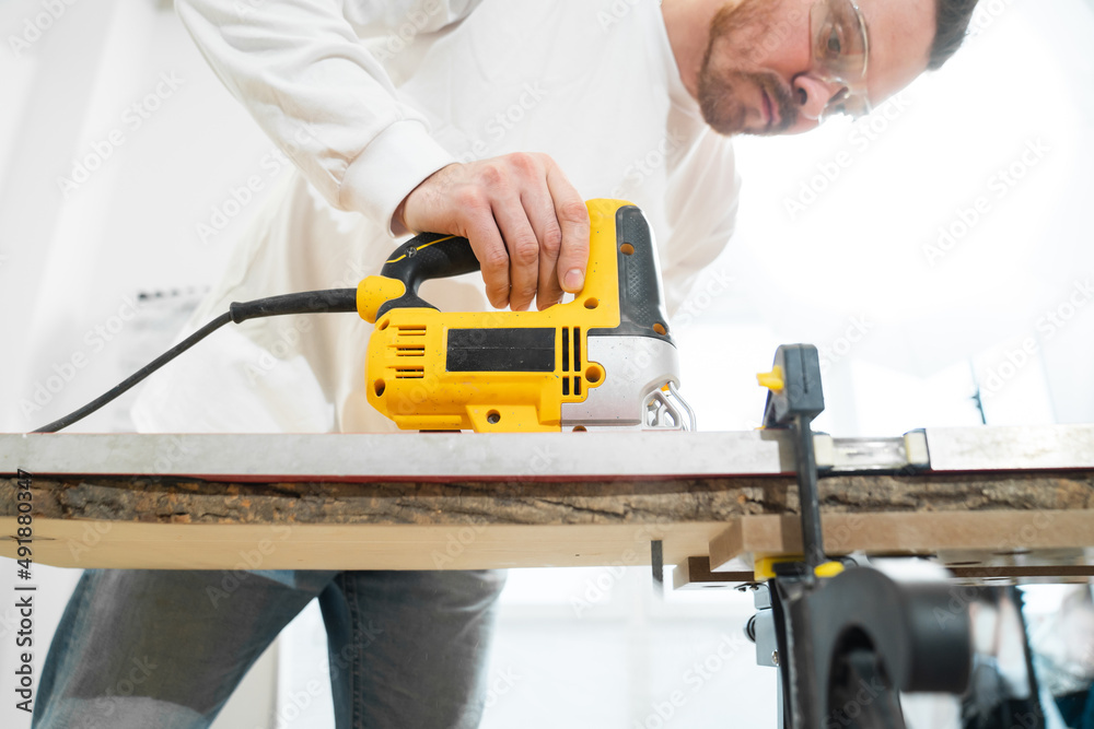 carpenter in protective gloves and glasses cuts wood with electric jigsaw carpenter in protective gloves and glasses cuts wood with electric jigsaw
