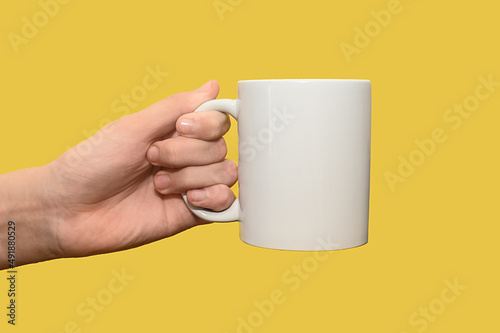 Close-up of a woman's hand holding an empty white mug. On a yellow background.