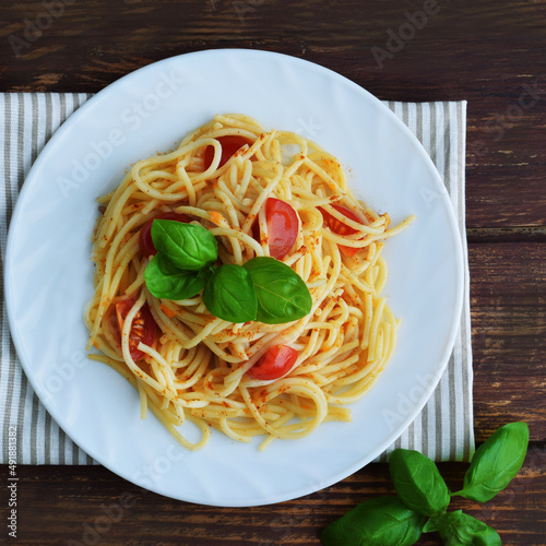 Spaghetti pasta with tomatoes and basil on a wooden table.