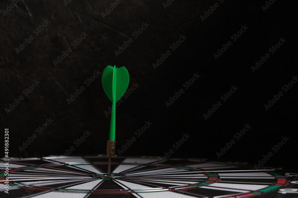Dartboard with green dart stuck in center. Dartboard with green dart stuck in center.