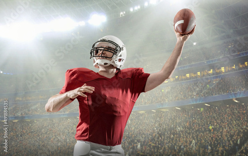 American football sportsman player with ball in action on stadium under lights of background. Sport, proud footballer in white helmet and red t-shirt ready to play.