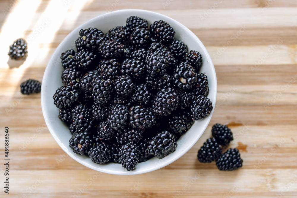 Blackberries in a white deep plate and on a wooden surface. Blackberry. Blackberry fruit close up on wooden table Blackberries in a white deep plate and on a wooden surface. Blackberry. Blackberry fruit close up on wooden table