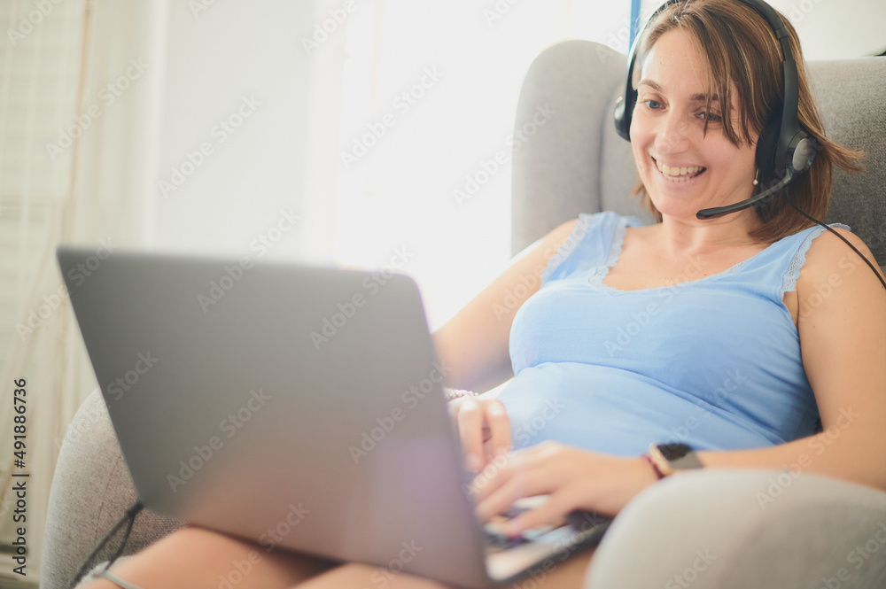 Young adult woman casually dressed, smiles while works from home using headphones and microphone to answer calls from clients, solving problems with a laptop. Young adult woman casually dressed, smiles while works from home using headphones and microphone to answer calls from clients, solving problems with a laptop.