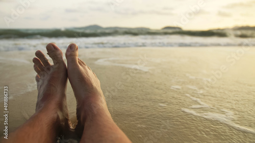 The barefoot man feet relaxed are lying on the sandy beach and washed by the water and foam of the ocean. Concept relax tropical resort traveling happy summer holiday