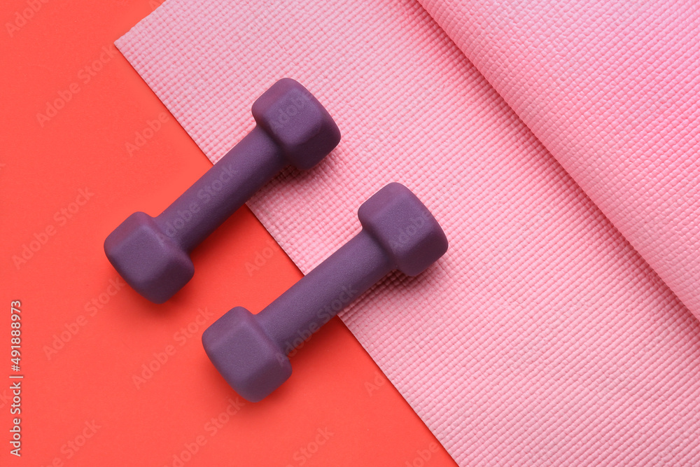 Stylish dumbbells and fitness mat on red background Stylish dumbbells and fitness mat on red background