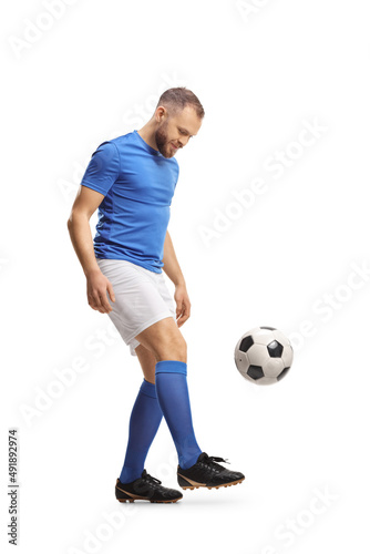 Full length shot of a footballer in a blue top and white shorts kicking a ball