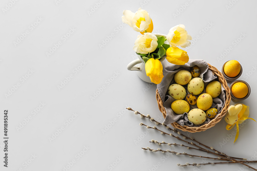 Basket with painted Easter eggs, tulip flowers and bunny on light background Basket with painted Easter eggs, tulip flowers and bunny on light background