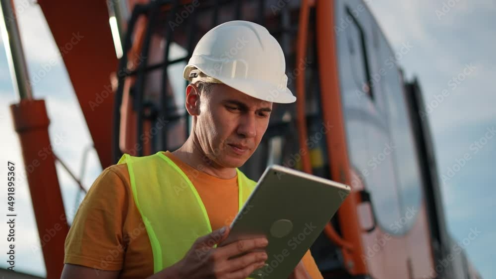worker in hard a hat with digital tablet near excavator. construction site driver business with online digital tablet. industry construction concept. worker hard hat near excavator truck in uniform. worker in hard a hat with digital tablet near excavator. construction site driver business with online digital tablet. industry construction concept. worker hard hat near excavator truck in uniform.