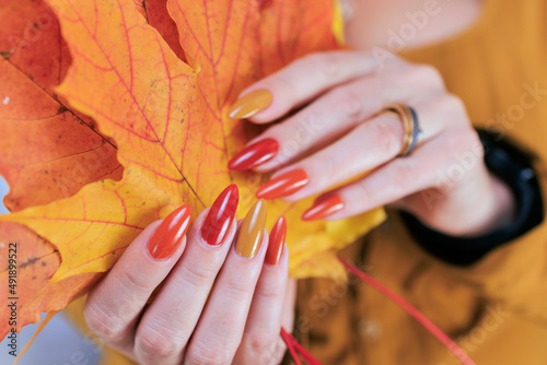 Murais de parede Female hand with long nails and a bottle of bright red orange yellow nail polish