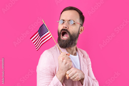 Portrait of a satisfied young man with a beard with an American flag on a red studio background. Great US patriot and defender of freedom.