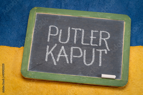 Putler kaput - sign against Russian attack on Ukraine, white chalk writing on a slate blackboard against paper abstract in color of Ukrainian national flag, blue and yellow photo
