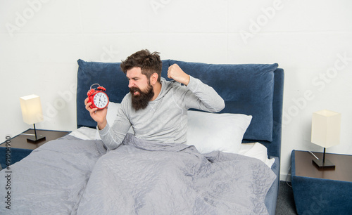Angry guy punching alarm clock being in bed in morning, overslept