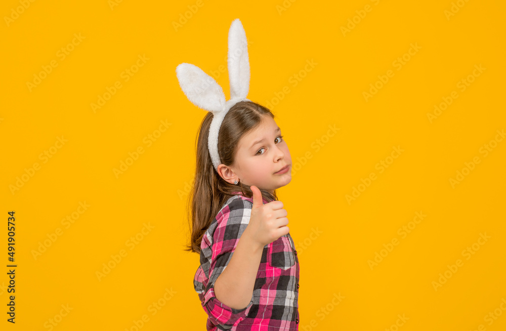 easter child in bunny ears on yellow background. thumb up easter child in bunny ears on yellow background. thumb up