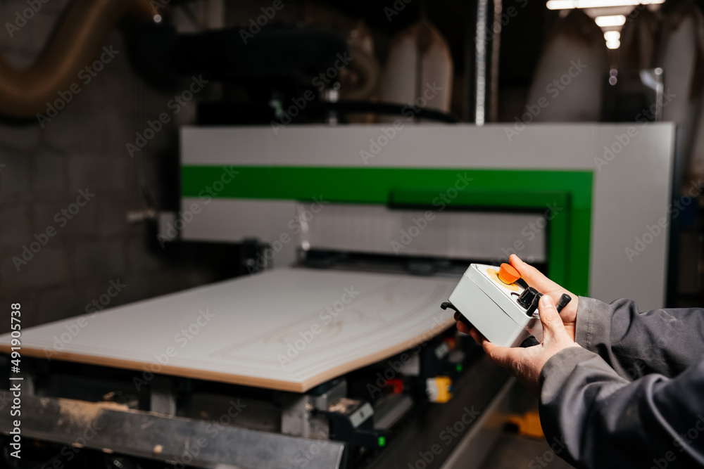 hands of the worker holding the control panel of the machine of processing of furniture accessories which is in the background hands of the worker holding the control panel of the machine of processing of furniture accessories which is in the background
