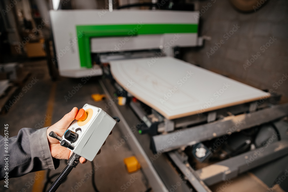 hands of the worker holding the control panel of the machine of processing of furniture accessories which is in the background hands of the worker holding the control panel of the machine of processing of furniture accessories which is in the background