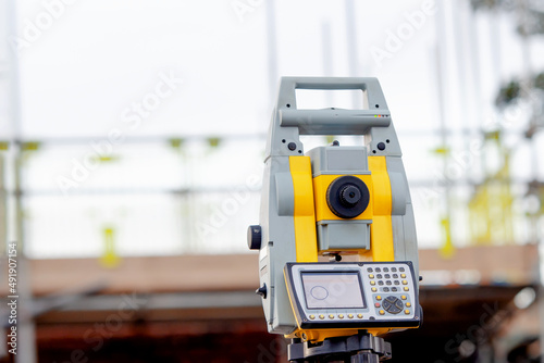 Yellow total station on tripod on building site against cloudless blue sky. Construction site and surveying equipment, tacheometer set out on tripod ready for setting out.
