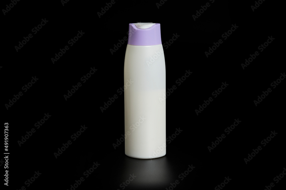 Unbranded bottle of shampoo, cream rinse, cream or beauty product with purple cap on black background with reflection below. Unbranded bottle of shampoo, cream rinse, cream or beauty product with purple cap on black background with reflection below.