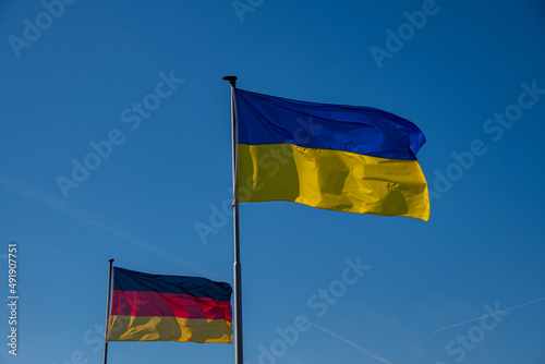 The Ukrainian flag and a German flag wave against a cloudless sky photo