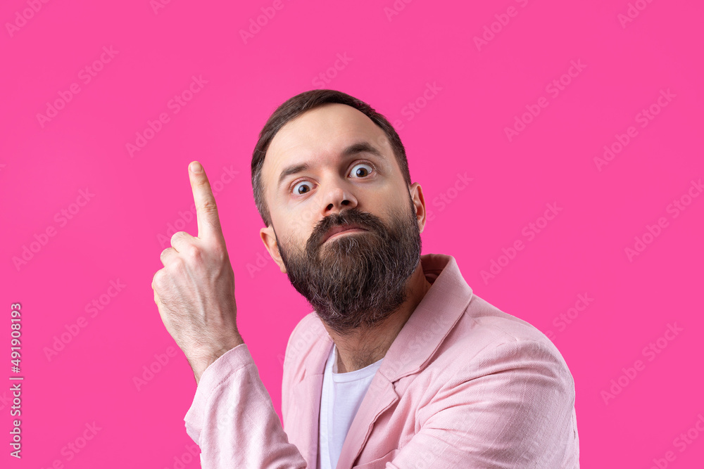 Handsome man with a beard in a pink jacket is thinking over an isolated red background. Handsome man with a beard in a pink jacket is thinking over an isolated red background.