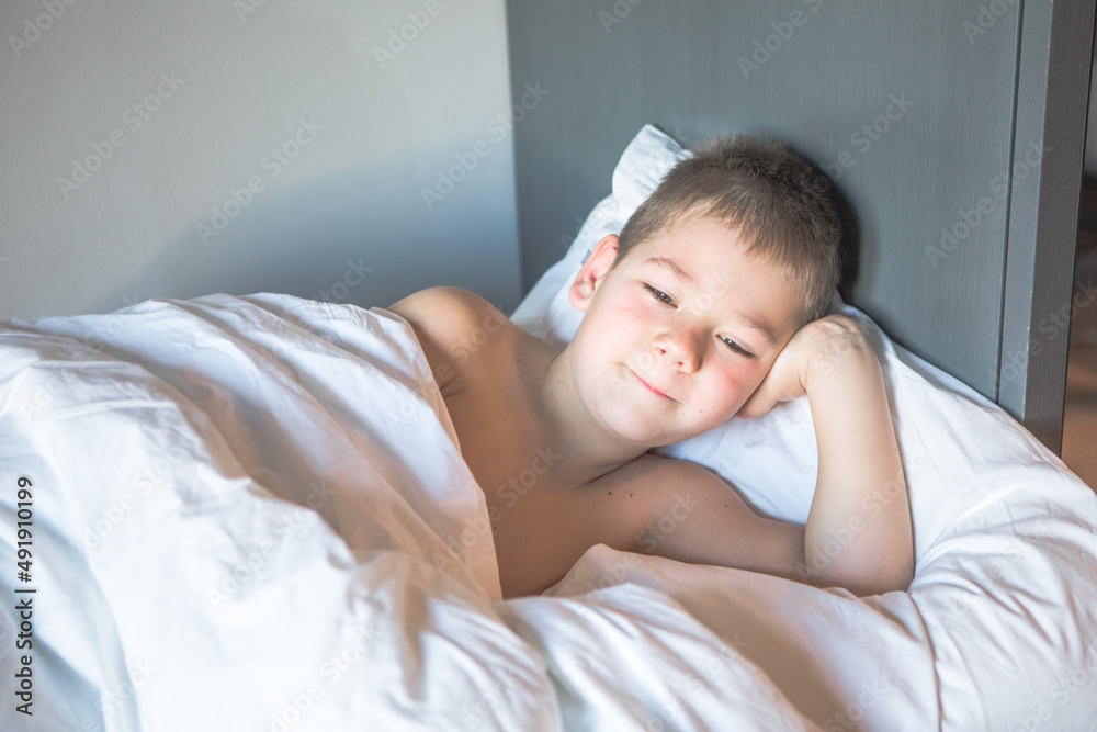 Kid 7 year old lying on bed, Sleepy child waking up the morning in his bed room with morning light, sad boy lies on a bed in the room Kid 7 year old lying on bed, Sleepy child waking up the morning in his bed room with morning light, sad boy lies on a bed in the room