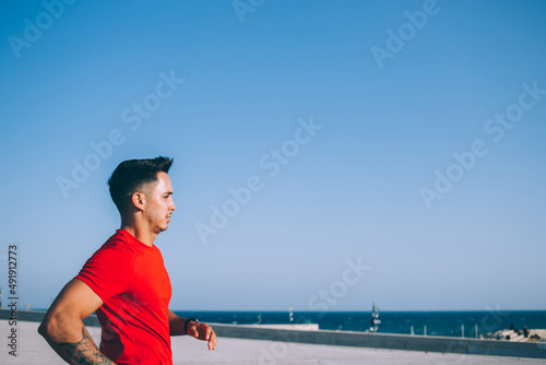 Side view of determined Caucasian triathlete preparing to marathon enjoying morning run sprinting, muscular male concentrated bodybuilder jogging with endurance during strength cardio training © BullRun