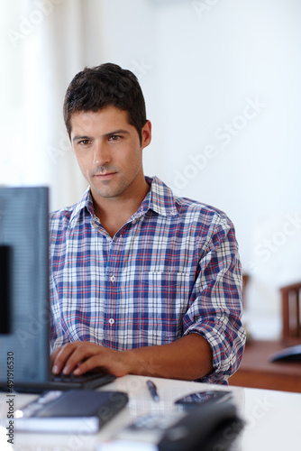 Hard at work. A young man concentrating while sitting at a desk in front of a computer.
