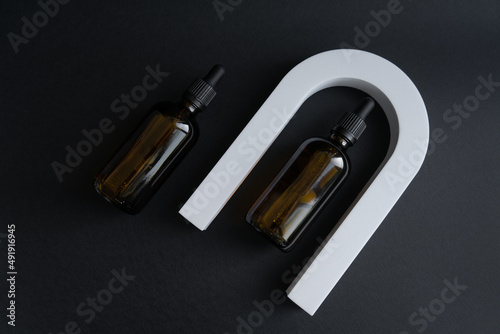 Cosmetic bottle made of dark amber glass without labels on a black background with geometric shapes. With place for your design. Minimalist brand packaging mockup.