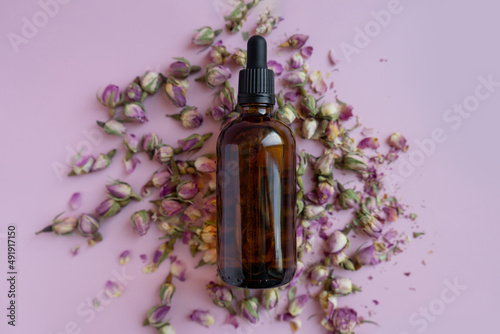 Minimal composition with face care cosmetic product on lilac background. flat lay. A dark bottle of serum lies on small flowers on a light background. Template for the packaging of cosmetics.